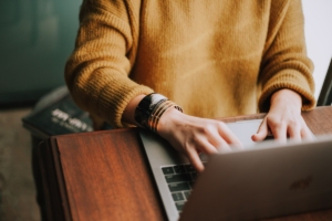 woman-wearing-yellow-sweater-bracelets-working-on-laptop