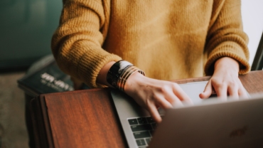 woman-wearing-yellow-sweater-bracelets-working-on-laptop